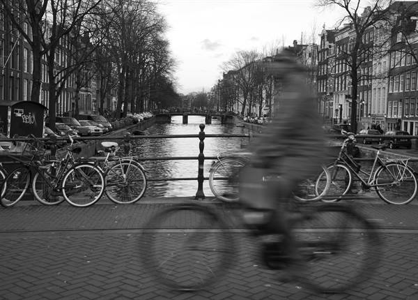 Blurred cyclist crosses a bridge with parked bicycles along an Amsterdam canal