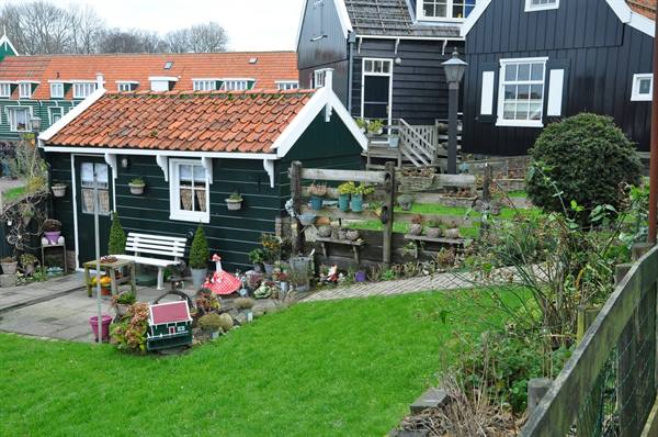 Green and black wooden houses with tile roofs, garden with bench and flower pots