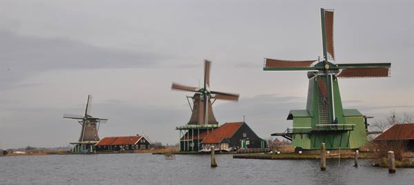 Green wooden windmills lined along the Zaan river at Zaanse Schans