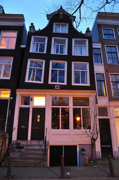 Bell-gabled Amsterdam canal house, dark brick, warm lit windows at dusk