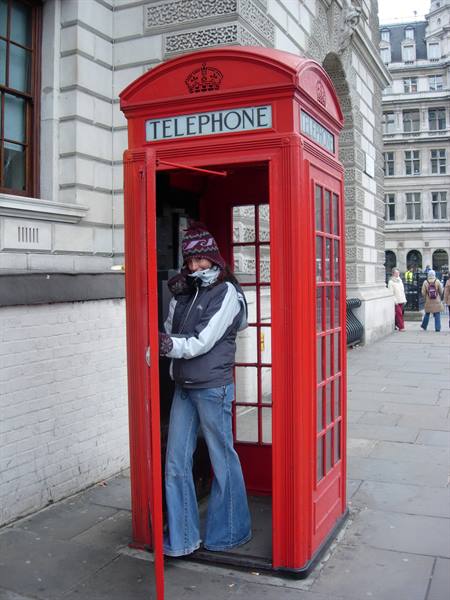 Tourist inside a red London telephone booth beside stone buildings