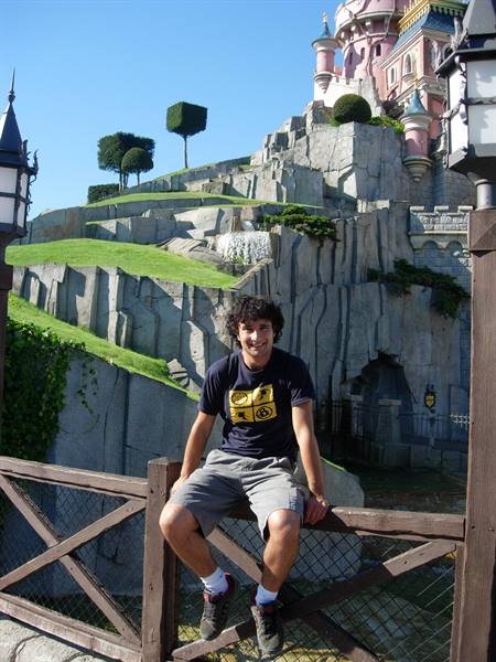 Young man sitting on a wooden fence in front of the Sleeping Beauty castle
