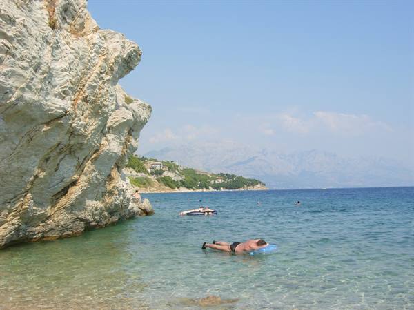 Swimmer on blue air mattress in rocky cove, turquoise water and mountains