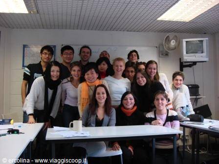 Smiling group of students in a classroom with whiteboard, wall TV and fan