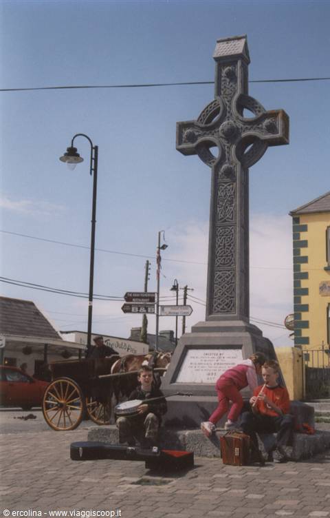Boys playing banjo at the base of the stone Celtic cross
