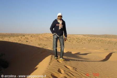 Man in white hat and scarf standing on a sand dune