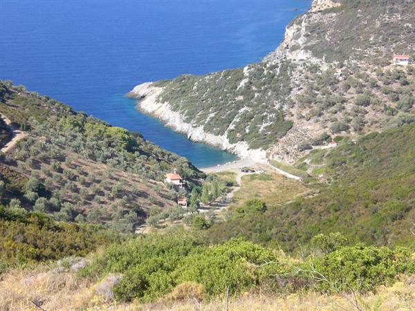 Cove with pebble beach between green hills, Mediterranean shrubs and rural houses