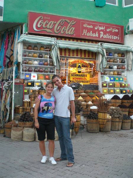 Couple in front of Habab patisserie with Coca-Cola sign among baskets and spices