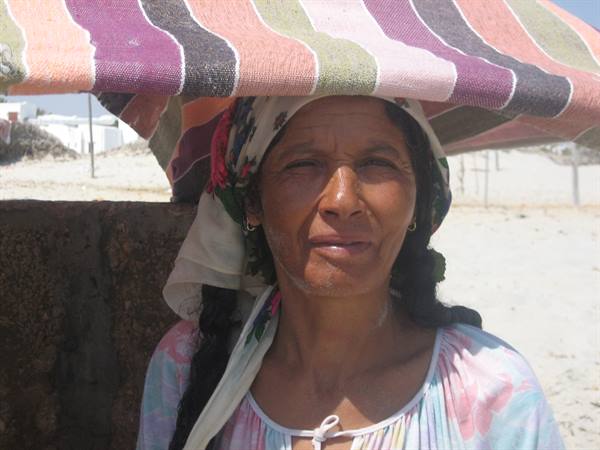 Woman with braid and headscarf under a striped beach umbrella