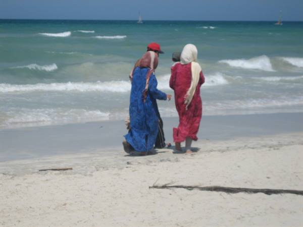 Veiled women in colorful robes walk along the sandy beach before the waves