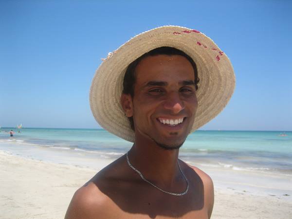Smiling man wearing straw hat and silver chain on the beach