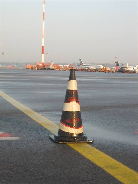 Traffic cone on wet tarmac, airport apron with Alitalia planes and antenna tower