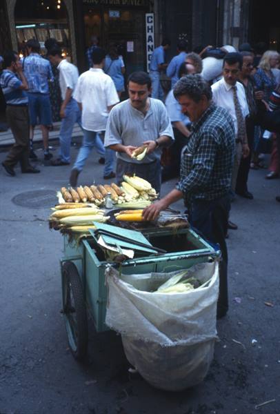Street vendor grilling corn cobs on his cart, crowded Istanbul street