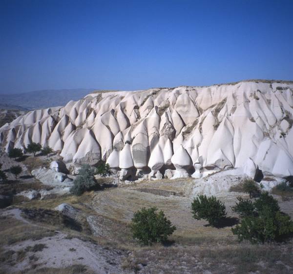 White eroded rock formations of Cappadocia among trees and blue sky
