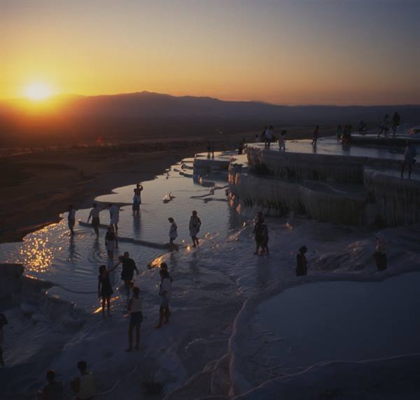 Tourists on Pamukkale travertine terraces at sunset
