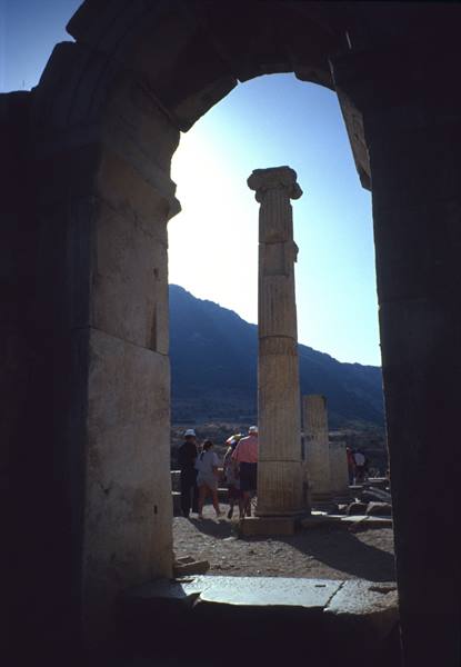 Marble column at Ephesus framed by a stone arch, tourists walking below