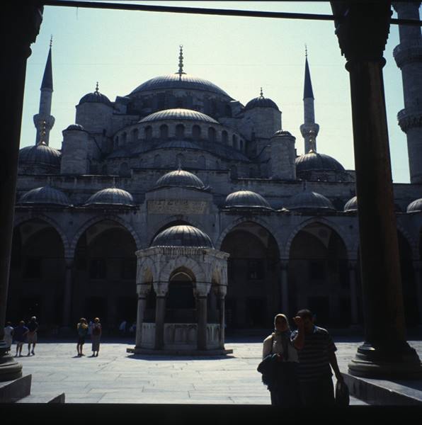 Blue Mosque, Istanbul: visitors in courtyard with fountain, domes and minarets backlit