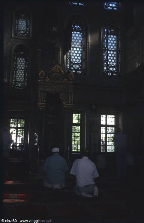 Two worshippers pray in dim light at the Blue Mosque mihrab, Istanbul