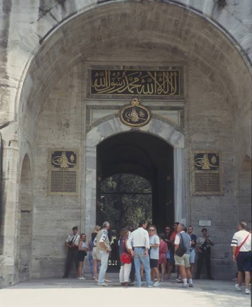 Tourists beneath the stone arch of Topkapı Palace, Istanbul, golden calligraphy inscription