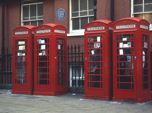 Four red telephone boxes lined up in front of a brick building in London