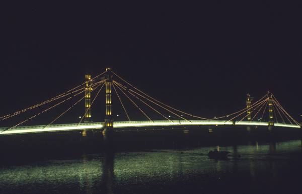 Illuminated suspension bridge over the Thames at night, golden lights on dark water