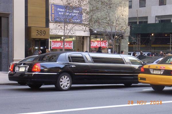 Black stretch limousine and yellow taxi on a city street with sample sale signs