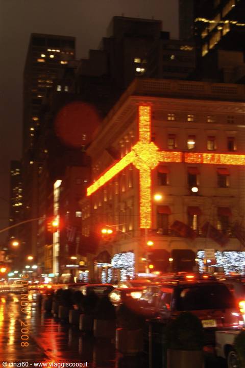 Giant red Christmas bow glowing on a facade, wet streets and traffic, New York