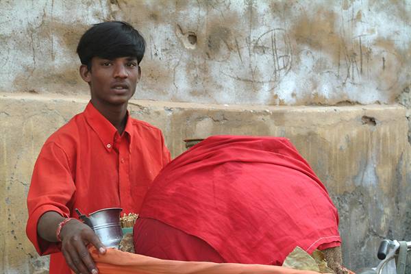 Boy in red shirt sells from metal cups beside a cloth-covered cart