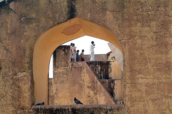 Tourists on stone stairs framed by ochre arch, pigeons nearby, Jantar Mantar