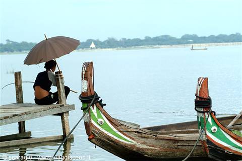 Fisherman with umbrella on wooden pier, green-painted wooden boats, Taungthaman lake