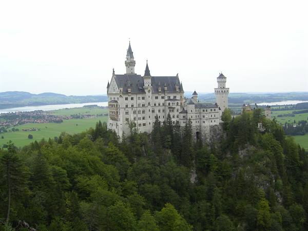 Neuschwanstein castle towers over a wooded rock among meadows and lakes
