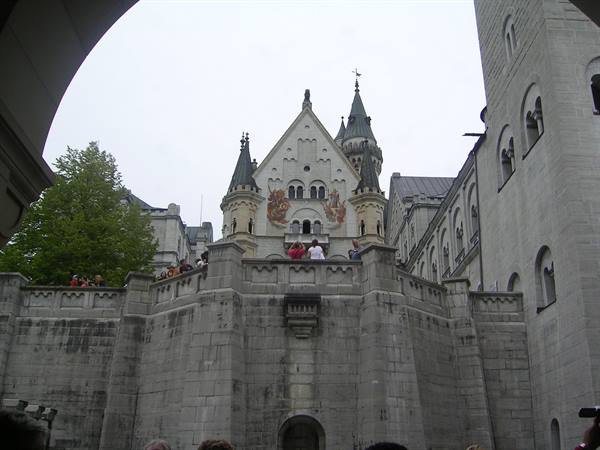 Tourists on the stone bastion of Neuschwanstein Castle, towers and murals under grey sky