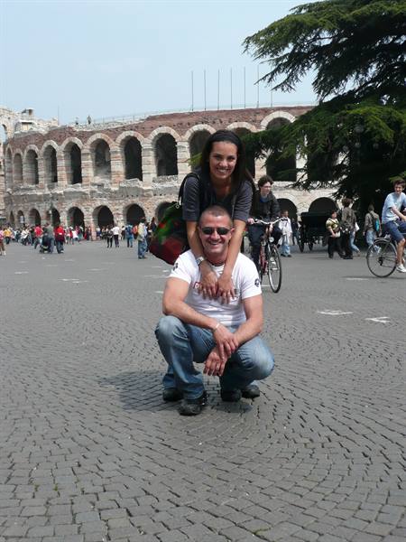 Smiling couple in front of Verona Arena, cobblestones and passing cyclists