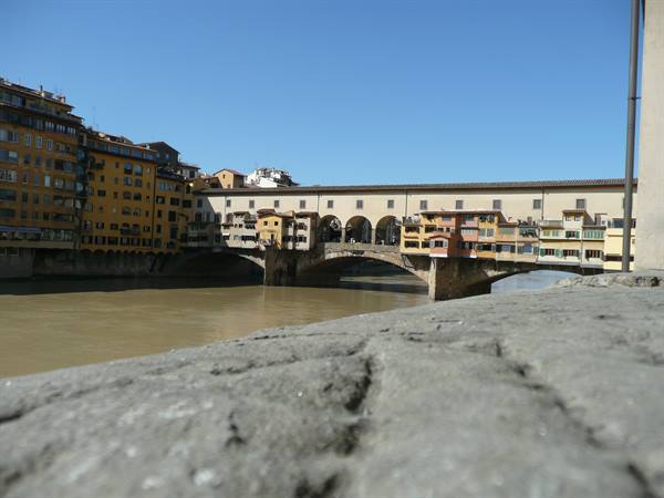Ponte Vecchio in Florence, colorful houses on the Arno bank under blue sky