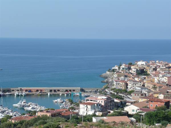 Marina with moored boats beneath a hillside village of colorful houses