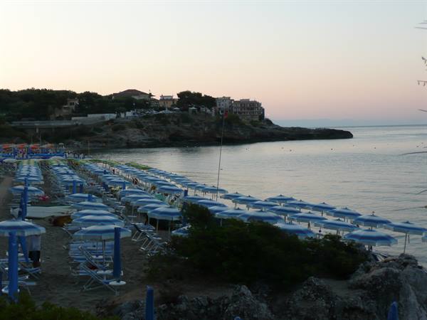 Rows of closed blue umbrellas on the beach at dawn, rocky bay and village