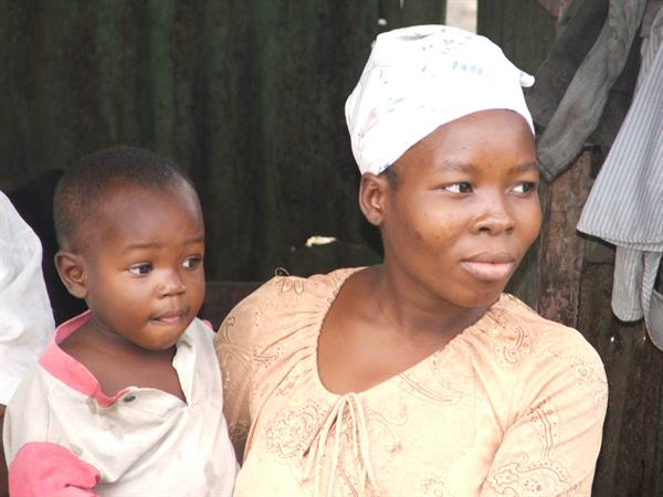 Woman in white headwrap with child in pink shirt by green wall