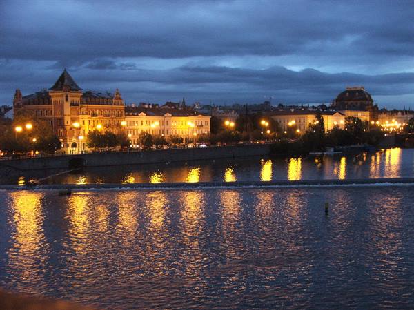 Illuminated buildings along the Vltava in Prague, golden lights reflecting on water