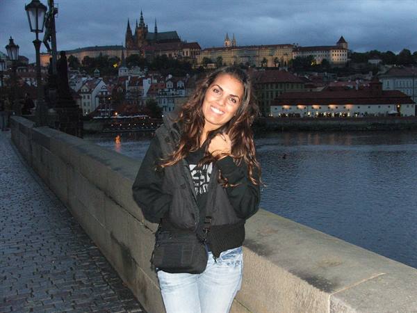 Smiling woman on Charles Bridge, Prague Castle visible at dusk behind