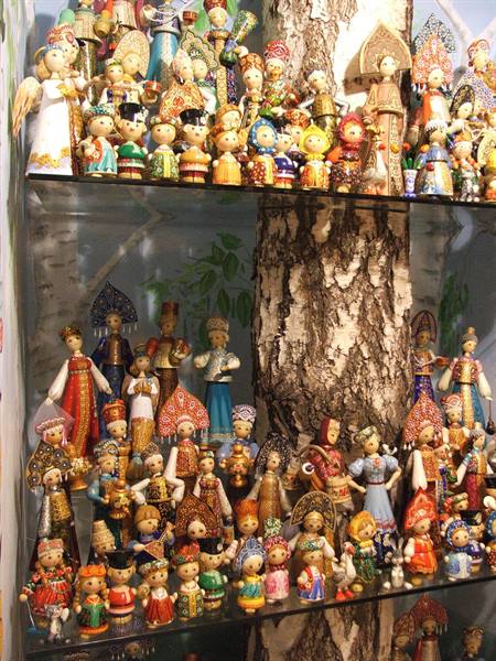 Hand-painted dolls in traditional Russian folk costumes on glass shelves around a birch trunk