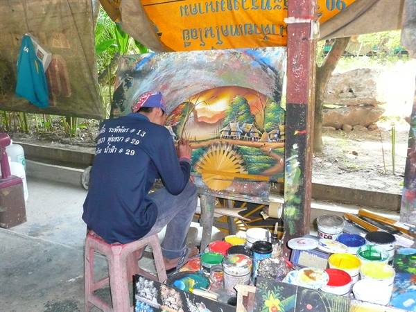 Street painter working on a village canvas among paint jars, Thailand