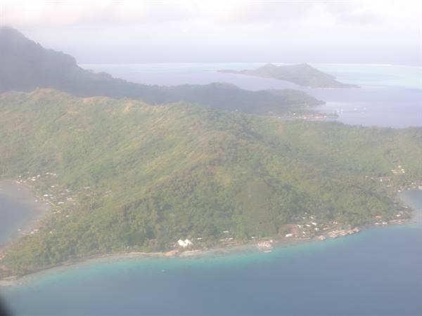 Green tropical island seen from plane, turquoise lagoon and coastal villages