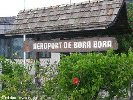 Wooden sign of Bora Bora Airport surrounded by green bushes and red flowers
