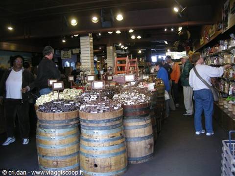 Shoppers browse wooden barrels filled with candy in a warm-lit store