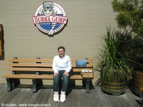 Smiling woman sitting on wooden bench under the Bubba Gump Shrimp sign