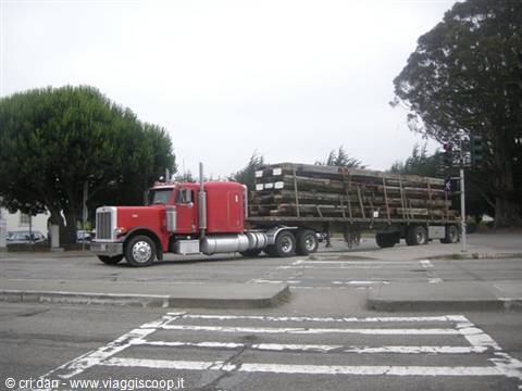 Red truck hauling wooden beams at a tree-lined intersection