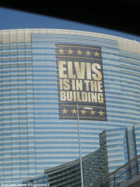 Glass skyscraper covered by a huge blue and gold banner reading "Elvis is in the building"