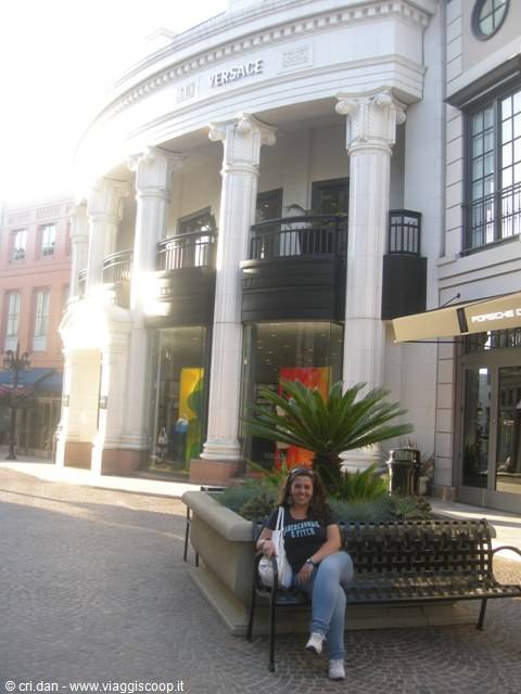Smiling woman on a bench in front of white-columned Versace boutique