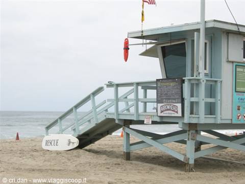 Light blue wooden lifeguard tower on the sand, rescue board and ocean under grey sky