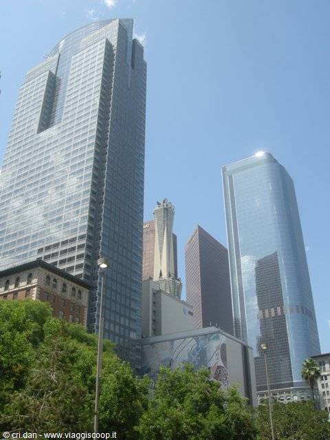 Glass skyscrapers above green trees, blue sky with a few clouds